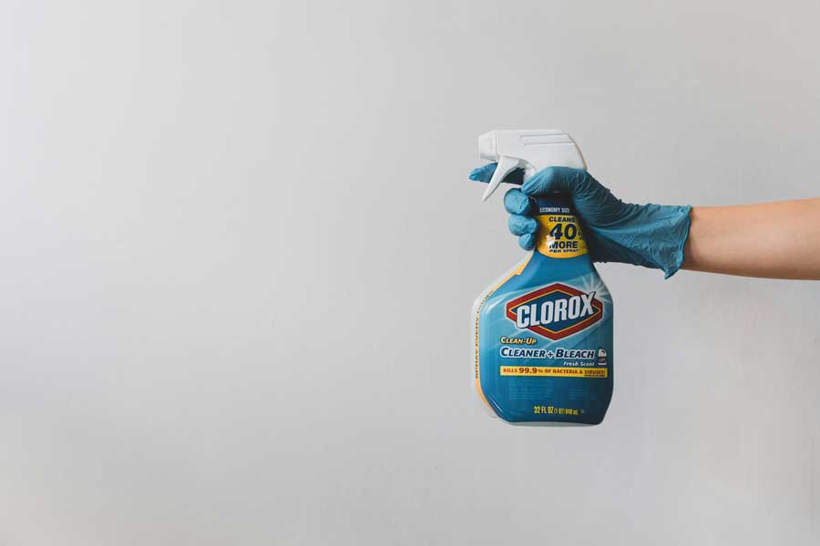Hand wearing blue glove holding Clorox cleaner spray bottle, representing chemical cleaning options for pet odor removal at home.