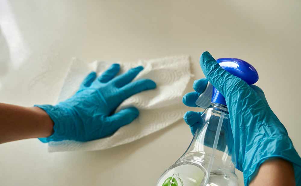 DIY cleaning vs. professional cleaning services—person wearing gloves using a spray bottle and cloth to clean a surface, representing the decision homeowners face between handling household cleaning themselves or hiring professionals, especially in humid areas like Jacksonville, Fleming Island, and Orange Park where maintenance demands can be higher.